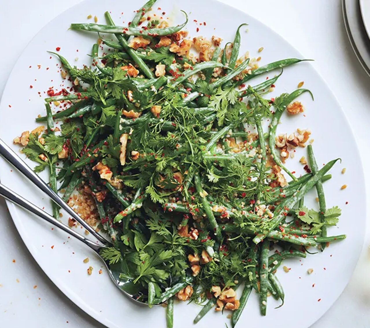 salade haricots verts, herbes avec une cuillère en métal dans un plat blanc