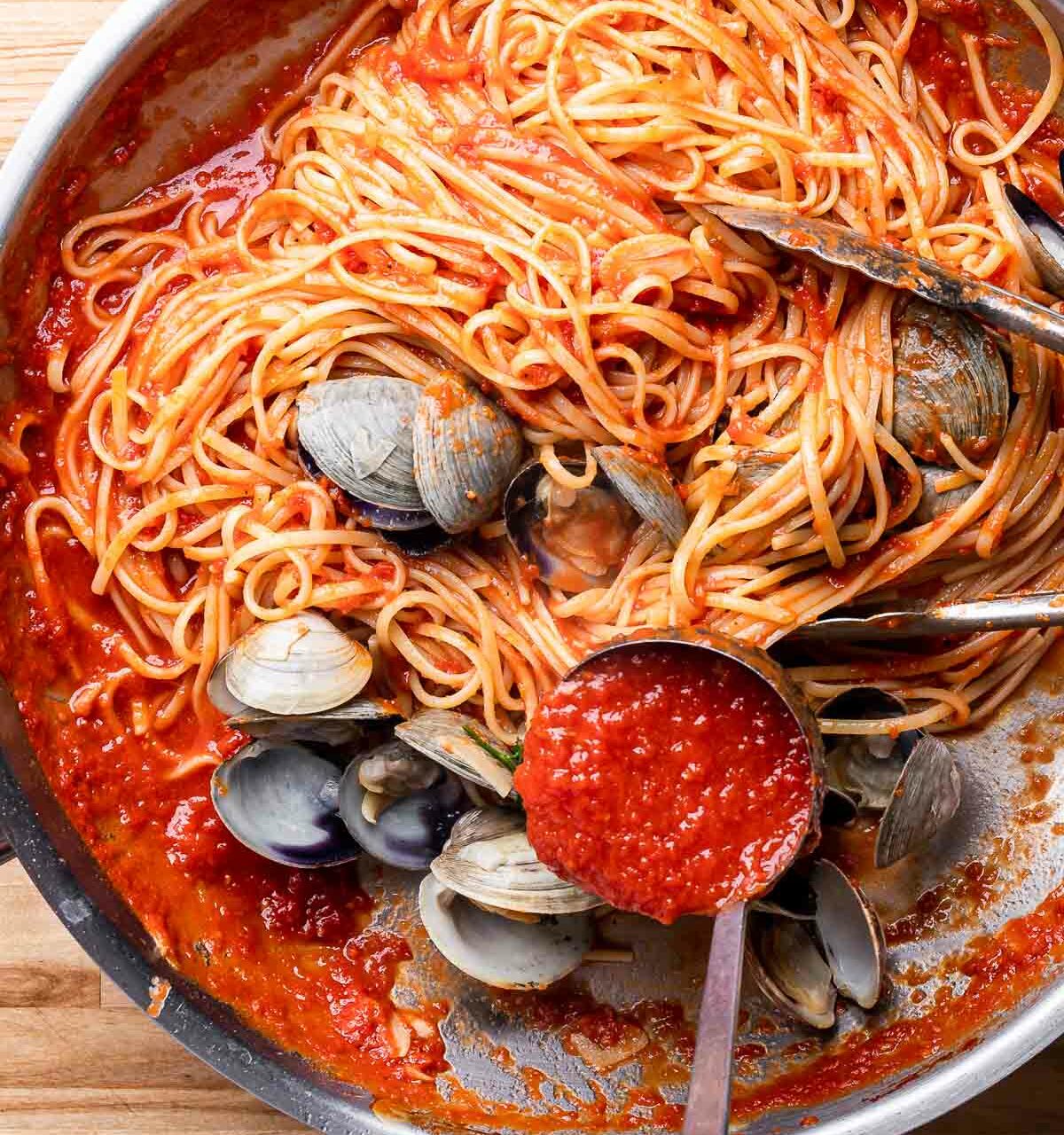 spaghetti aux palourdes et à la tomate dans une poêle avec une louche pour servir