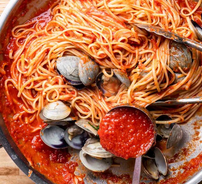 spaghetti aux palourdes et à la tomate dans une poêle avec une louche pour servir